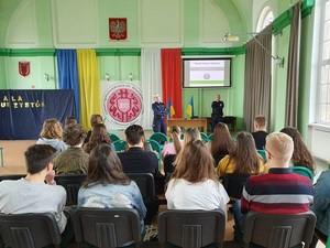 policjant z wizytą w szkole, sala szkolna, siedząca młodzież, flagi