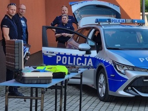 policjanci umundurowani stojący przy oznakowanym radiowozie