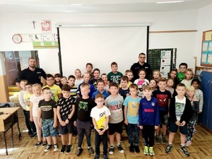 dwóch policjantów umundurowanych stojących wraz z dziećmi w klasie szkolnej