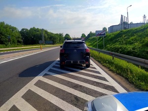 samochód citroen koloru ciemnego stojący na drodze przy znaku koniec obszaru zabudowanego