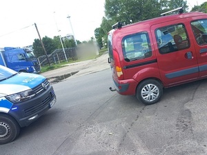 dwa pojazdy przy drodze, oznakowany radiowóz oraz czerwony Renault Kangoo