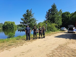 policjant i strażacy stoją przy akwenie wodnym