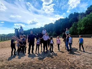Na piasku stoi umundurowany policjant, dzieci oraz konie. Światło dzienne