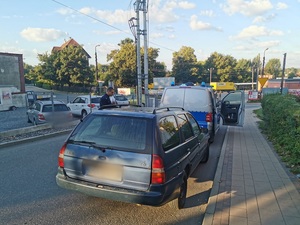 samochód osobowy, niebieski na ulicy, przed nim radiowóz, obok umundurowany policjant