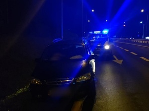noc, droga, samochód osobowy ciemny za nim radiowóz oznakowany, bus na sygnałach