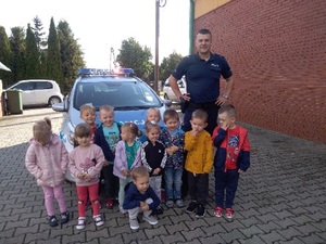 policjant umundurowany wraz z grupa dzieci stoją przy radiowozie