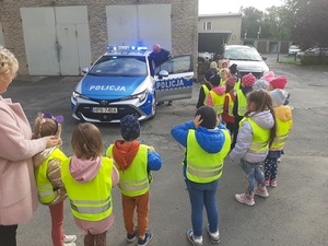 dzieci stoją na dworze, radiowóz obok którego stoi policjant
