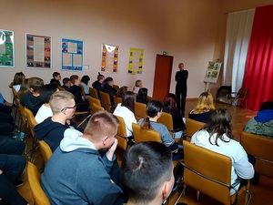 policjantka stoi na sali, młodzież siedzi