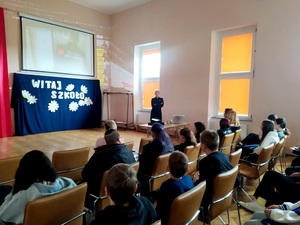 policjantka stoi na sali, młodzież siedzi z tyłu widoczny obraz z rzutnika