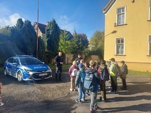 dzieci stoją przed budynkiem wraz z policjantami w mundurach przy oznakowanym radiowozie