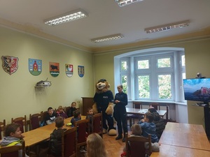 dzieci siedzą w sali przy stołach, w tle policjantka i Komisarz Lew