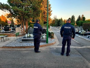 dwóch umundurowanych policjantów stoi na cmentarzu