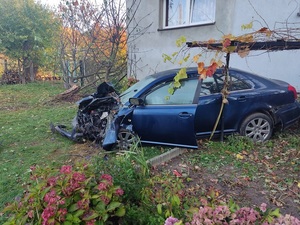 uszkodzony samochód koloru ciemnego stoi na trawie przy ścianie budynku