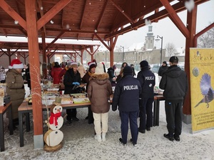 stoiska drewniane na zewnątrz, śnieg, osoby stoją , dwóch umundurowanych policjantów przy stoisku