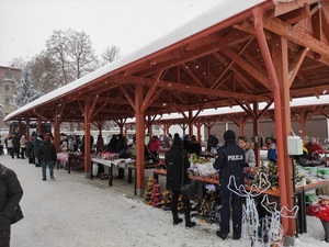 stoiska drewniane na zewnątrz, śnieg, osoby stoją , dwóch umundurowanych policjantów przy stoisku
