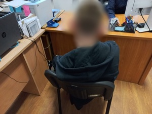 mężczyzna w ciemnej bluzie siedzi tyłem na krześle przed biurkiem w pomieszczeniu