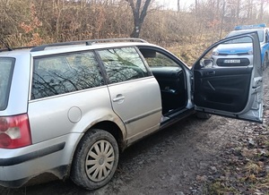 srebrny samochód kombi z otwartymi drzwiami na drodze gruntowej, w tle radiowóz
