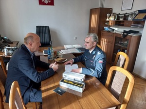 policjant wraz z mężczyzną ubranym w ciemny garnitur siedzą naprzeciw siebie przy stole w pomieszczeniu