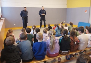 policjanci umundurowani stoją naprzeciwko dzieci siedzących w klasie