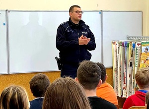 policjant stoi przy tablicy przodem do dzieci w ławkach