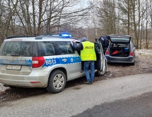 2 pojazdy osobowe, w tym jeden oznakowany radiowóz stające na gruntowej, leśnej drodze
