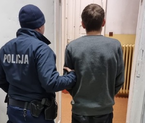 umundurowany policjant prowadzi zatrzymanego