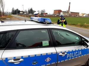 policjant umundurowany stoi przy radiowozie z ręcznym miernikiem prędkości