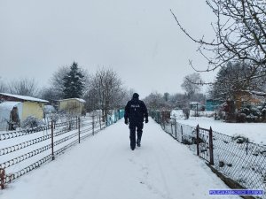 policjant umundurowany  idzie po śniegu w dzień, wzdłuż siatka ogrodzeniowa