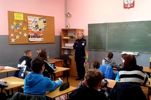 policjant w klasie lekcyjnej, umundurowany przed nim tyłem dzieci w ławkach