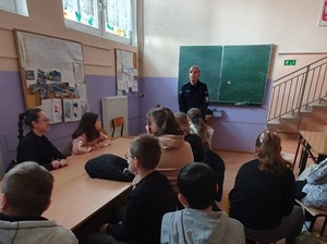 policjant w klasie lekcyjnej, umundurowany przed nim tyłem dzieci w ławkach