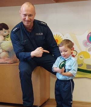 umundurowany policjant wskazuje palcem na dziecko trzymające w ręce tarczę do zatrzymywania pojazdów