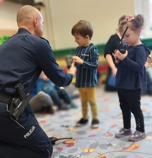 umundurowany policjant siedzi przed dziećmi pokazując im przedmioty