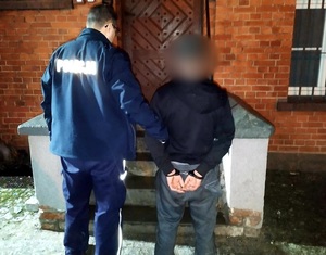 mężczyzna w kajdankach prowadzony przez umundurowanego policjanta