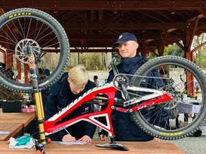 dwóch policjantów umundurowanych toi za stołem, na którym stoi rower koloru bialo-czerwonego