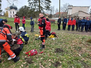 straż pożarna i ratownicy opatrują osoby cywilne przy namiotach, w tle stojąca młodzież