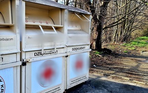 2 kontenery koloru jasnego na używaną odzież, stojące przy drodze gruntowej przy drzewach, dzień