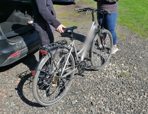 rower stojący obok samochodów na drodze szutrowej, widoczne nogi w spodniach dwóch osób