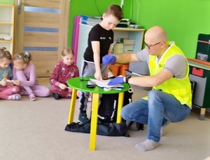 mężczyzna w kamizelce odblaskowej przy stoliku obok dzieci