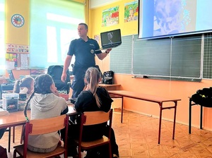 umundurowany policjant rozmawia z dziećmi siedzącymi w ławkach w klasie