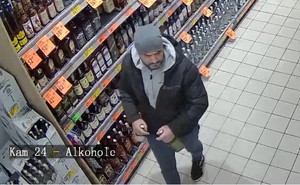 mężczyzna w szarej czapce, ubrany na ciemno, pod kurtą szara bluza z kapturem na terenie sklepu spożywczego