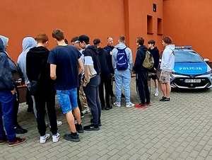 policjanci przy stołach, w tle radiowóz, przed umundurowanymi policjantami stoi młodzież
