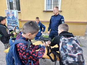 dzieci i młodzież na placu z policjantem, baner z policjantami z tyłu