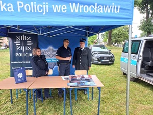 Policjanci wspólnie z strażakiem stoją przy stołach pod niebieskim  namiotem komendy wojewódzkiej