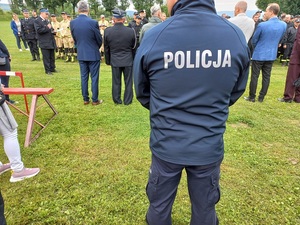 Policjant odwrócony tyłem stoi na trawie na zawodach Ochotniczych Straży Pożarnych