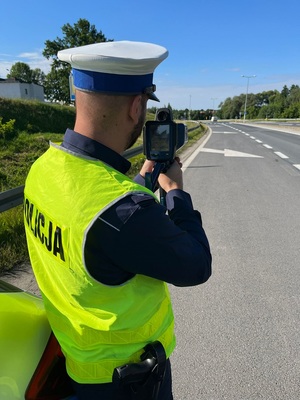 policjant w kamizelce odblaskowej dokonujący pomiaru prędkosći