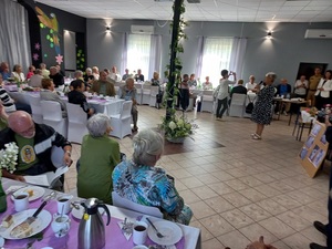 seniorzy siedzą przy stołach na spotkaniu w świetlicy wiejskiej w Laskach