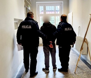 zatrzymany mężczyzna prowadzony przez 2 funkcjonariuszy policji