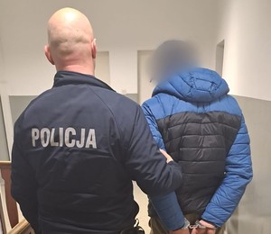 zatrzymany mężczyzna w kurtce, skuty z tyłu prowadzony przez umundurowanego policjanta
