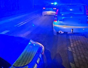 samochód Fiat Panda stojący na drodze, przed nim radiowóz na sygnałach, noc i niebieska poświata