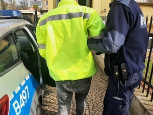 nietrzeźwy mężczyzna wyprowadzany z radiowozu przez umundurowanego policjanta w kierunku komendy